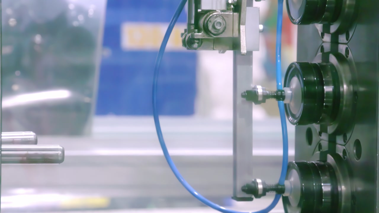 Close up of an automated industrial machine with blue pneumatic tubes, rollers and metal parts. Factory process scene showing precision engineering, mechanical movement and production technology.