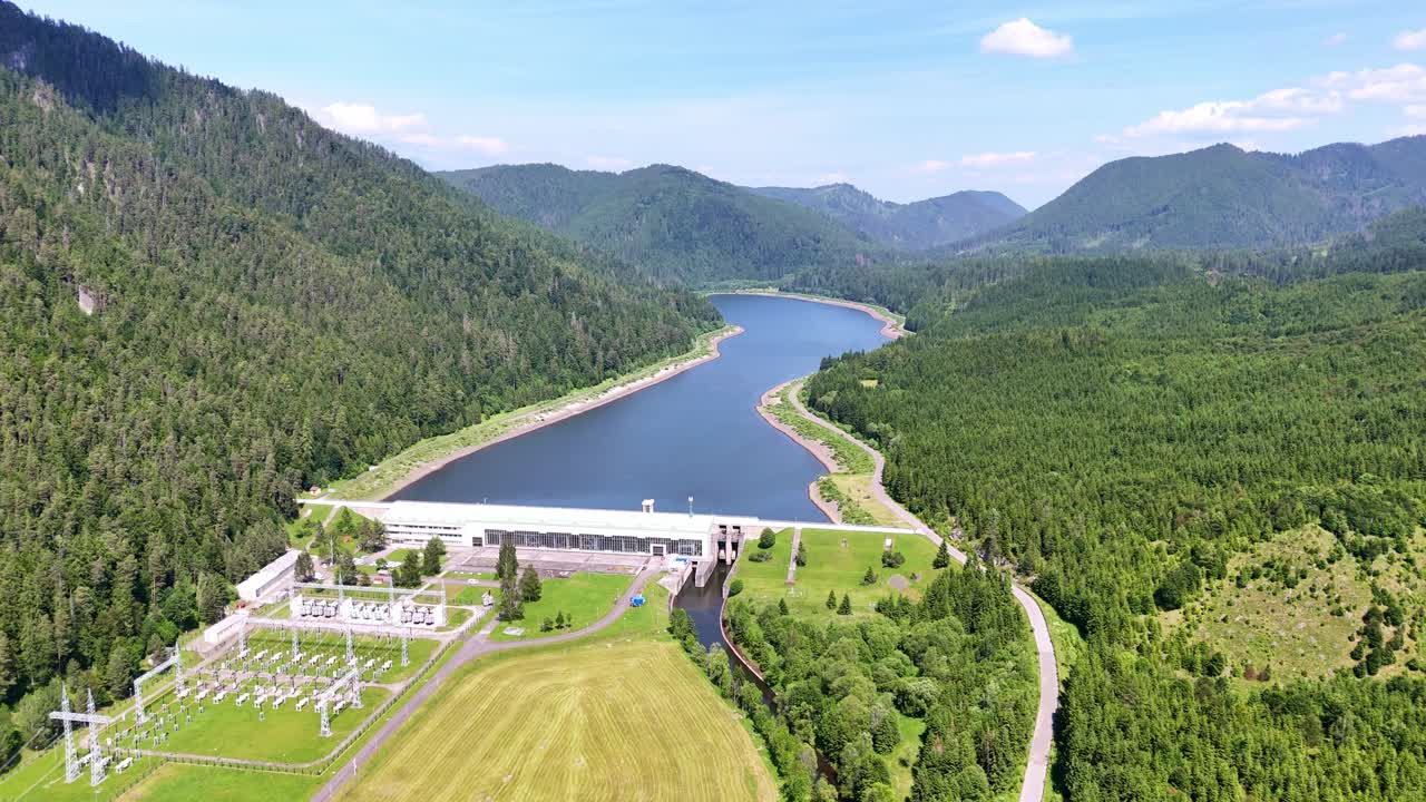 Drone circling sideways around Čierny Váh dam, showing the curved reservoir, green forested hills, and mountain scenery on a bright summer day in Slovakia