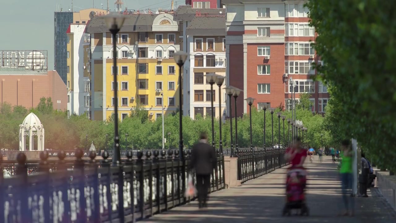 Kajen vid floden Isjim, människor går längs vattnet timelapse, byggnader, lokaler, trottoar och träd. Solig dag. Astana, Kazakstan