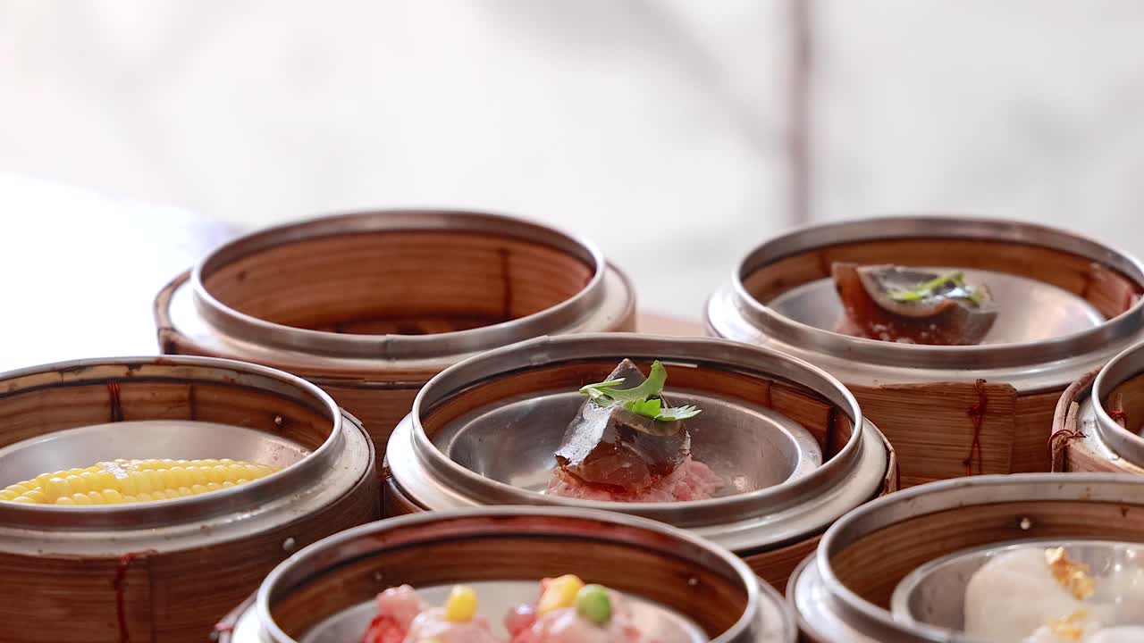 Hands arrange dim sum baskets in a bright setting, showcasing traditional culinary preparation with vibrant ingredients and careful presentation