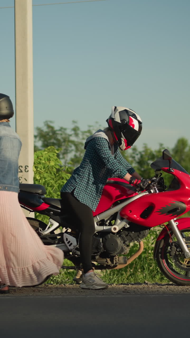 두 명의 여성이 헬을 착용하고, 하나는 빨간색 스포츠 자전거에 앉아 있고 다른 하나는 자전거에서 떨어집니다. 그들은 배경에서 지나가는 자동차와 함께 도로 에 있습니다.