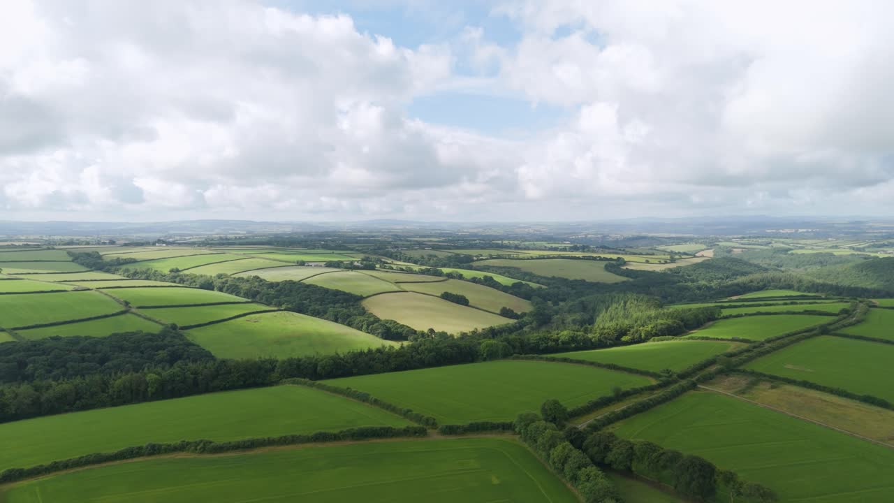 Aerial view capturing the expansive, lush green landscape of Devon, showcasing rolling hills and a patchwork of fields, United Kingdom
