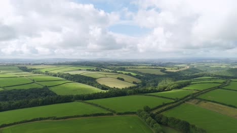 Aerial-view-capturing-the-expansive,-lush-green-landscape-of-Devon,-showcasing-rolling-hills-and-a-patchwork-of-fields,-United-Kingdom