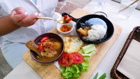 person eating chicken curry with rice and vegetables