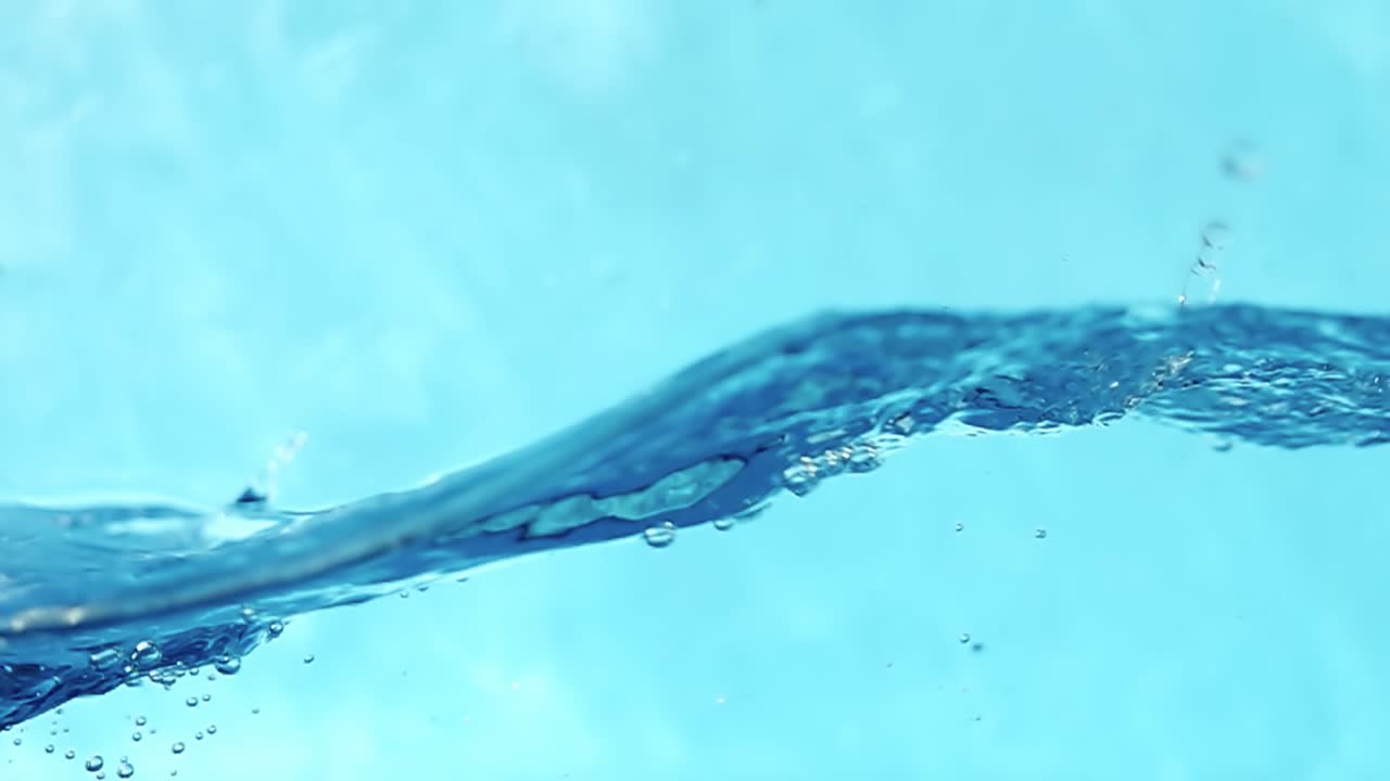 Slow motion  4k video of water waves with splashes and falling drops on a blue background. Studio shooting.