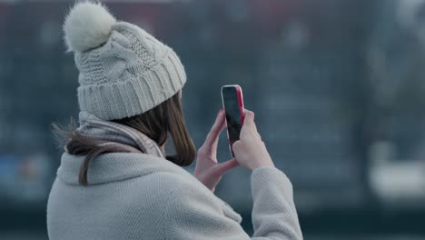 girl wearing winter cloth taking photo with her mobile phone in street