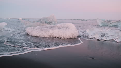 Handgehaltener-Schwenk-Von-Wellen,-Die-Eisbrocken-Am-Diamond-Beach,-Island,-Umspülen