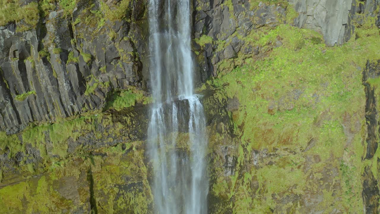 un dron sigue el agua en cascada por una cascada sobre un acantilado verde y amarillo