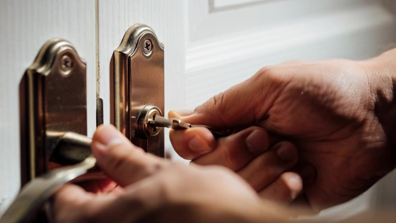 Inserendo la chiave con la mano destra, la mano sinistra che tiene ferma la maniglia sulla porta bianca, sbloccando il chiavistello, braccia nude.