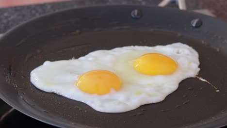 dos huevos enteros cocinados en una sartén en la parte superior de la estufa eléctrica todavía disparados