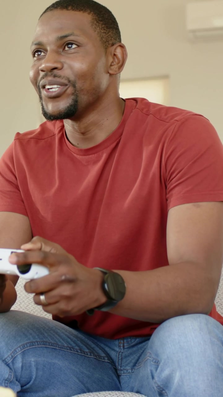 Vertical video: Reacting to game on screen, man in red shirt pressing white gamepad buttons at home