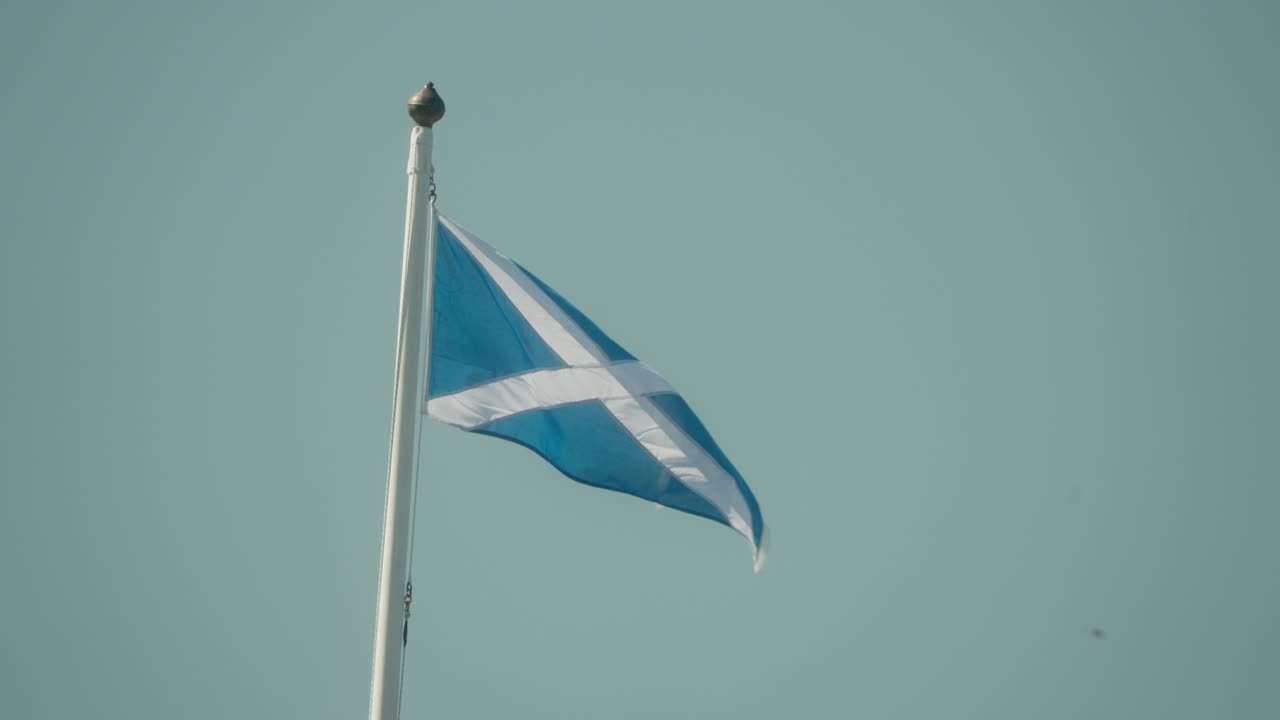 Scottish flag flying on a tall pole against clear blue sky. Symbol of national pride, heritage, and identity. Captured in high quality slow motion