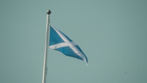 scottish flag flying on a tall pole against clear blue sky. symbol of national pride, heritage, and identity. captured in high quality slow motion