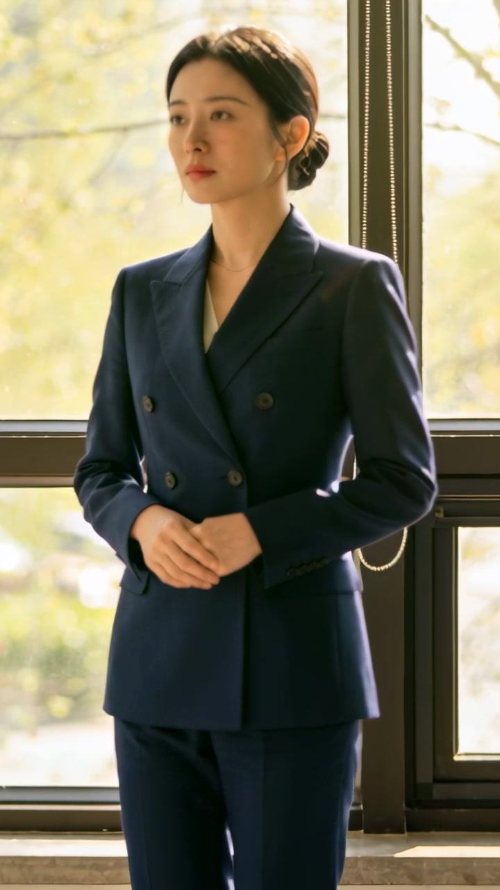 Vertical video: Noticing movement, woman shifting gaze at window wearing navy double-breasted suit