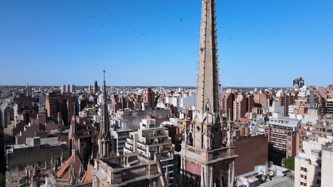 고밀도 시내 도시 경관을 내려다보는 공중 촬영, 높은 첨탑에서 내려오는 받침대는 코르도바 시에 있는 예수의 신성한 심장인 카푸치노 교회의 뾰족한 고딕 건축 세부 사항을 보여줍니다.