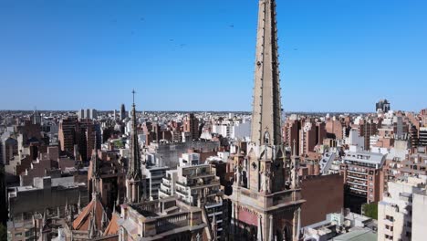 Aerial-shot-overlooking-at-high-density-downtown-cityscape,-pedestal-down-from-tall-spire-reveals-pointed-gothic-architecture-details-of-church-of-capuchinos,-Sacred-Heart-of-Jesus-at-Cordoba-city