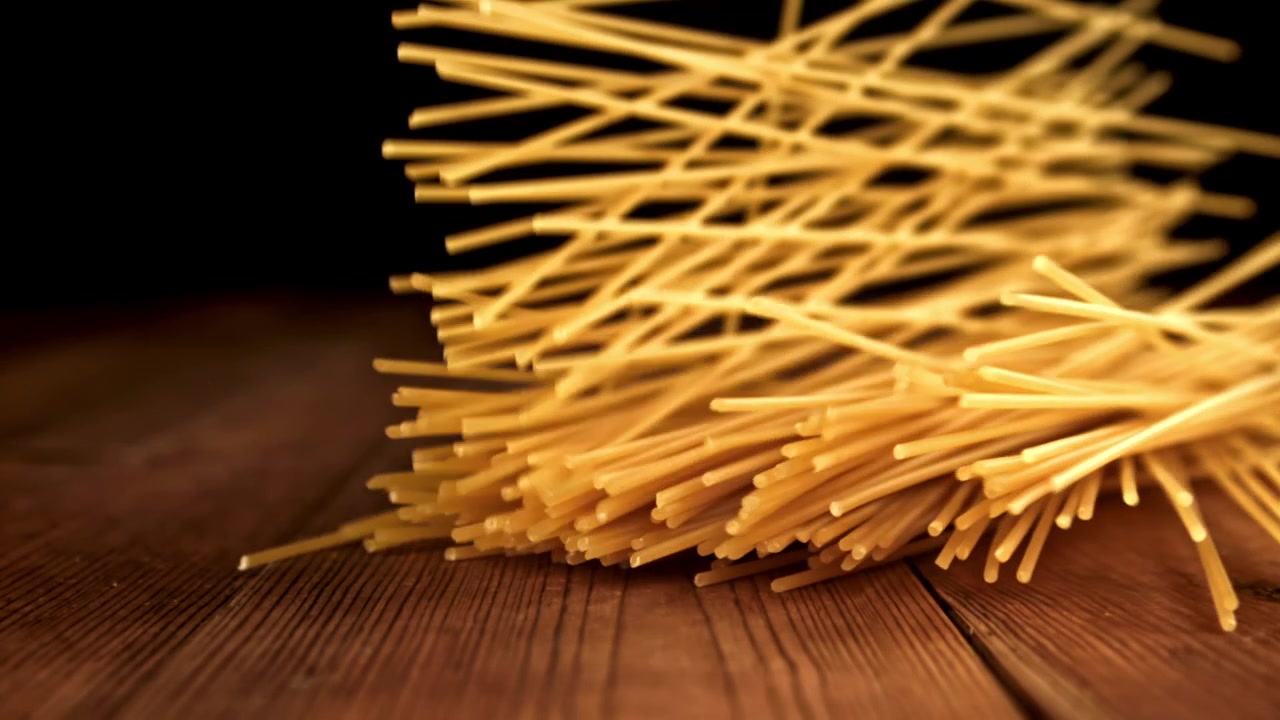 Spaghetti secchi che cadono al rallentatore su un tavolo di legno rustico
