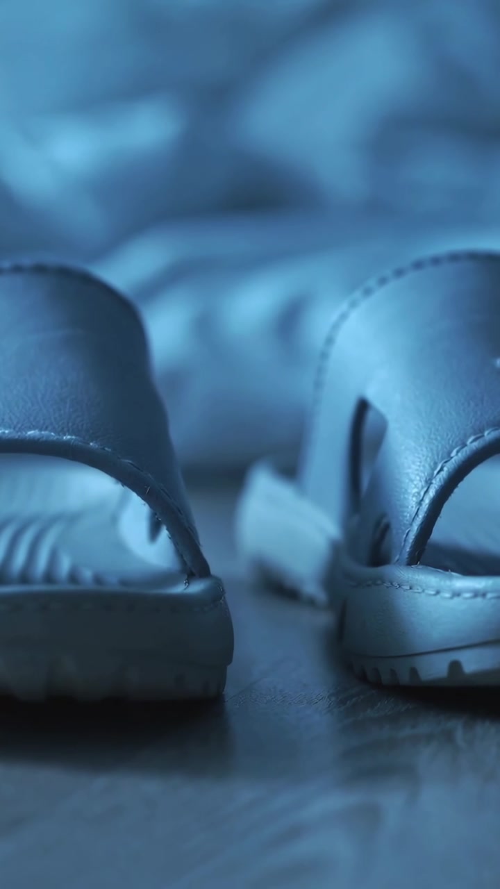 Video verticale: Telecamera che riprende due sandali slip-on appoggiati sul pavimento vicino al letto per un catalogo.