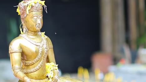 a golden statue is decorated with yellow petals, highlighting its intricate details and serene expression.