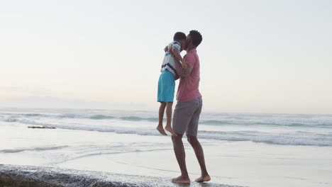 padre afroamericano llevando a su hijo en una playa soleada