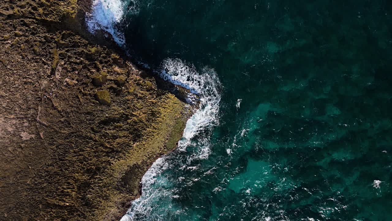 Drone em descida vertical sobre uma ponta rochosa irregular e pontiaguda no oceano com vista para o recife sob águas claras