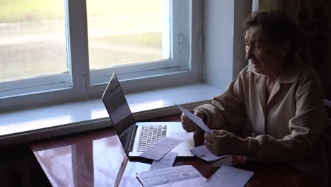 a very old woman sits at a table and checks bills for an apartment