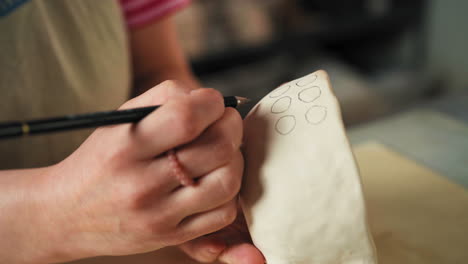 the person is sketching circular patterns on a ceramic cup with a pencil - close up