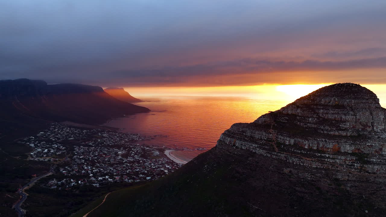 Cinematic aerial view of Table Mountain in Cape Town, South Africa, dramatic rocky cliffs with coastal cityscape at sunset, clouds rolling over peaks and golden evening light