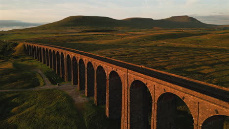 establishing drone shot of ribblehead viaduct with ingleborough in background at golden hour