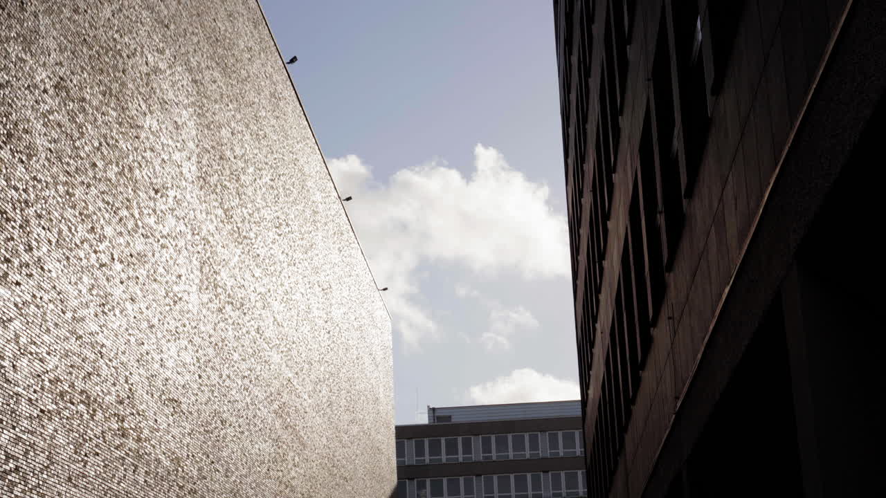 른의 극적인 도시 골목으로 반사적인 건축물, 대조적인 빛과 그림자, 부드러운 구름으로 밝은 하늘을 특징으로합니다.