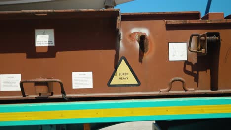 the camera glides from a 'super heavy' sign affixed to a truck platform, revealing a boat perched atop the sturdy transport