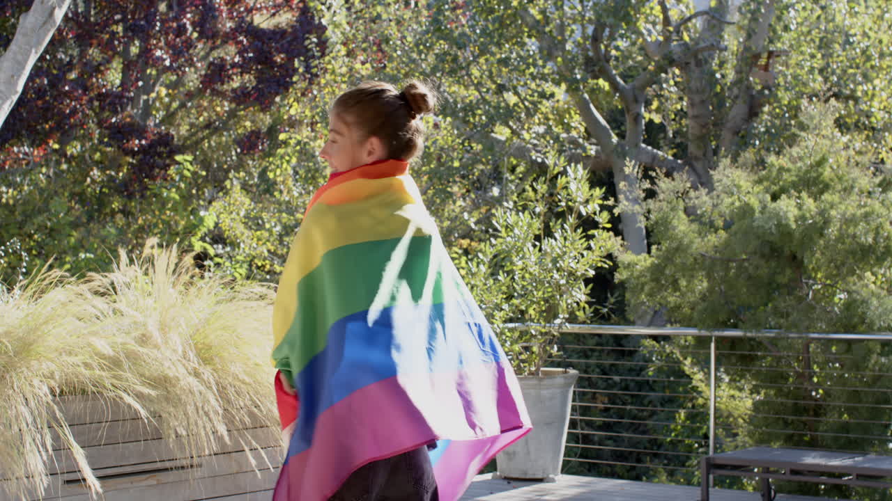 Wearing rainbow flag, person standing outside on sunny day, celebrating pride