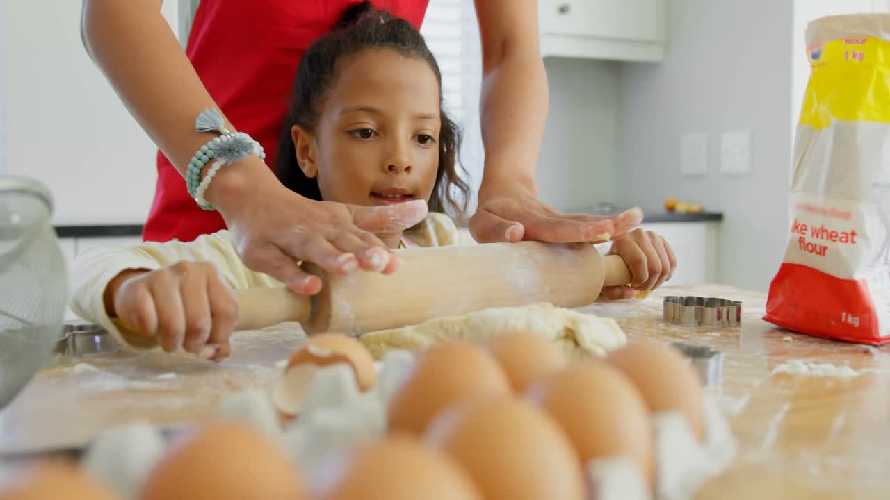 Black mother and daughter rolling dough with rolling pin at home 4k