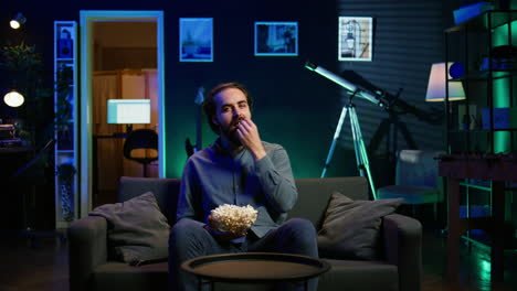 man turning on tv using remote control, eating popcorn