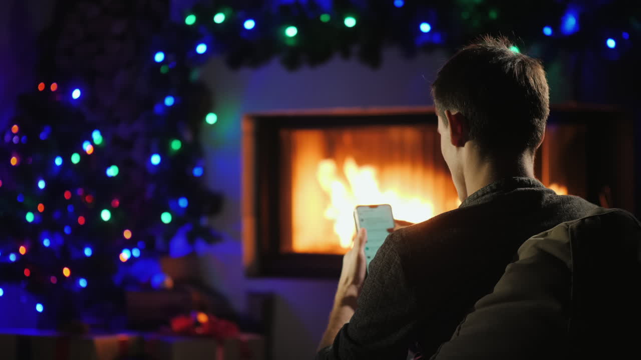 el joven usa un teléfono inteligente junto a la chimenea decorado para navidad