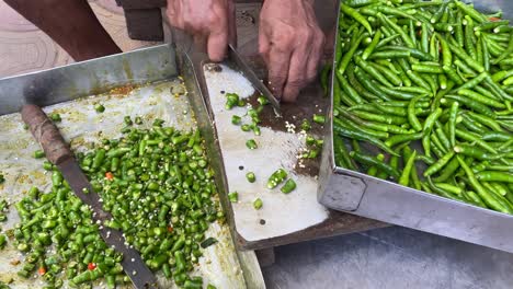 a poor man is shown up close using an iron knife to chop a lot of green chilies or mirchi at a roadside dhaba