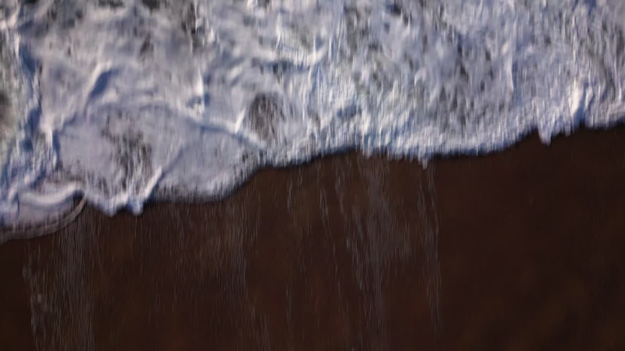 The camera of a drone flying from a sandy beach reveals the stormy waves of the ocean