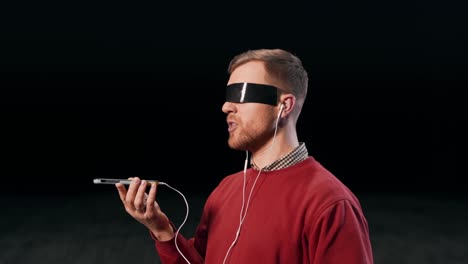 un hombre agradable con auriculares habla en un teléfono inteligente por mensaje de voz con ojos pegados