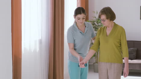 elder woman holding a dumbbell raising an arm up assisted by a female doctor 1