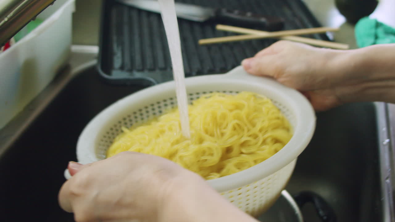 Korean mother pouring cold water onto jjolmyeon Korean noodles after boiling and tossing noodles in a colander