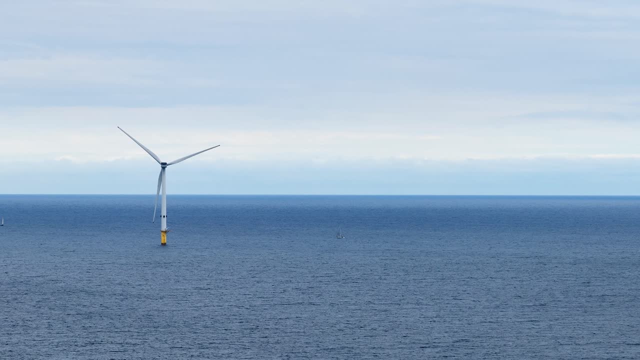 Single offshore wind turbine spins steadily in calm daylight over the North Sea, viewed from a fixed wide shot near Whitley Bay, England