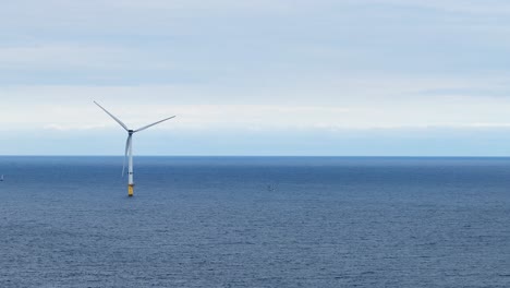 single offshore wind turbine spins steadily in calm daylight over the north sea, viewed from a fixed wide shot near whitley bay, england
