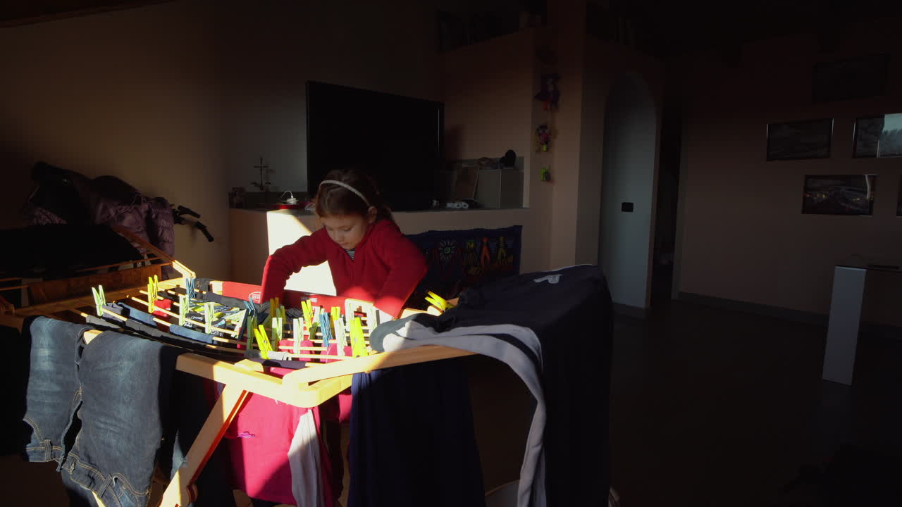 niña pequeña cuelga ropa en el tendedero en casa