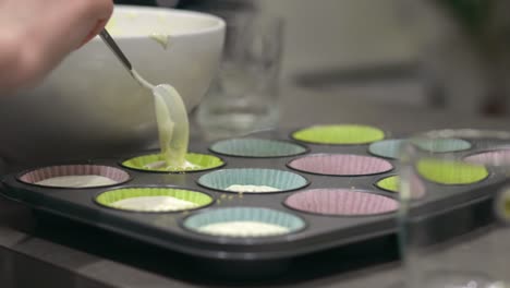 a woman scooping cheesecake cream filling with a spoon to fill mini muffin holders, which sit in a muffin pan, to make cheesecake cups