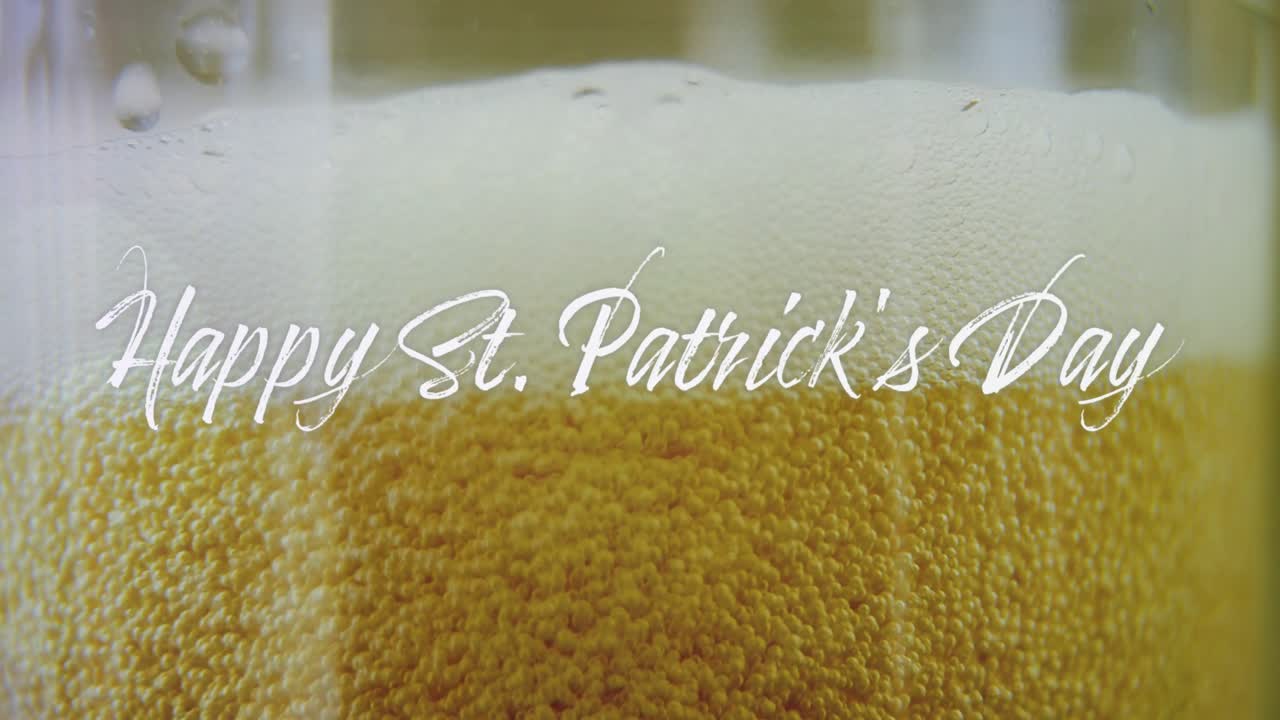 Nahaufnahme einer Kameraöffnung, bernsteinfarbenes Bier mit aufsteigenden Bläschen und sich setzendem Schaum, Text blendet für den St. Patrick's Day aus.