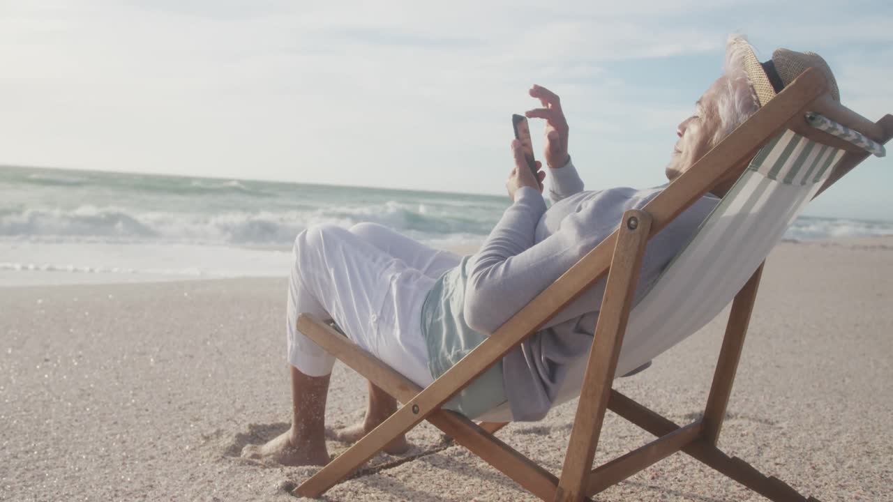 히스패닉 성인 여성이 해가 지는 해변에서 휴식을 취하고 스마트폰을 사용하고 있습니다.