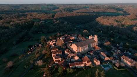Aerial-shot-of-a-small-village-and-its-church-in-the-middle-of-the-forest-at-sunrise,-Saint-Avit-Ségnieur,-Dordogne
