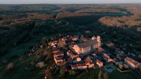 Toma-Aérea-De-Un-Pequeño-Pueblo-Y-Su-Iglesia-En-Medio-Del-Bosque-Al-Amanecer,-Saint-avit-ségnieur,-Dordoña