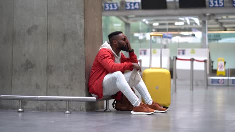 tired black tourist man on a long night connection at airport, waiting for plane sitting in terminal