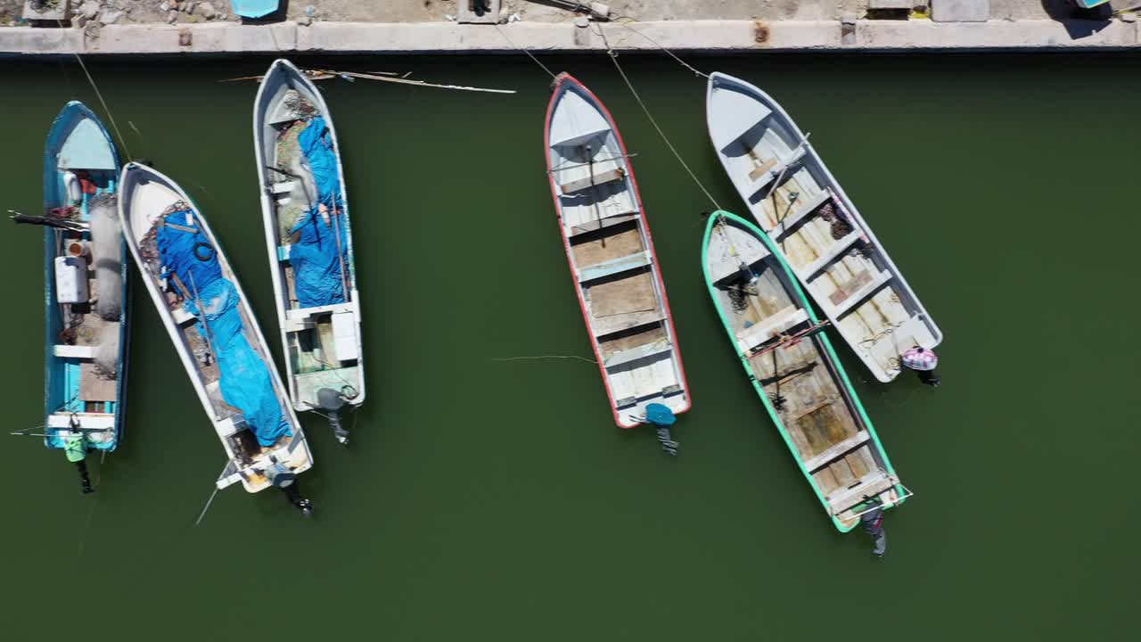 vista aérea mirando directamente hacia abajo y la cámara deslizándose hacia la derecha mostrando pequeños barcos pesqueros de madera en un puerto en méxico
